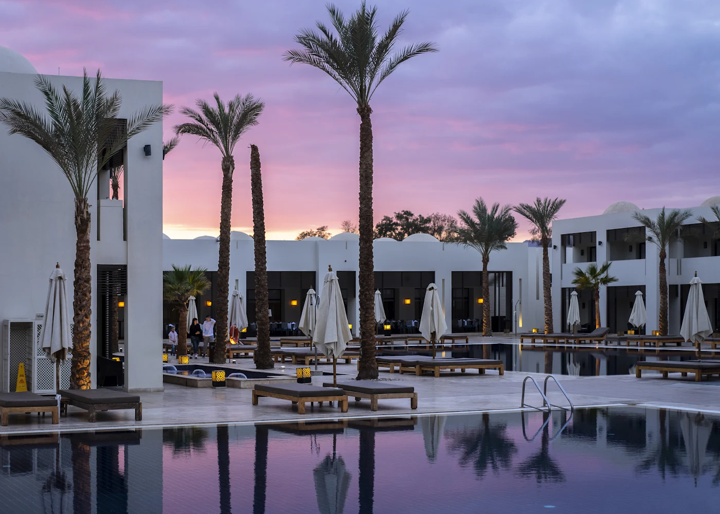 Uvendra exterior with palm trees and pool at dusk